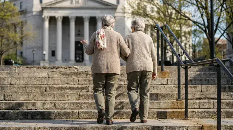 An older woman walking up wide stone steps beside another woman, seen from behind